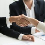 two people shaking hands in front of a laptop
